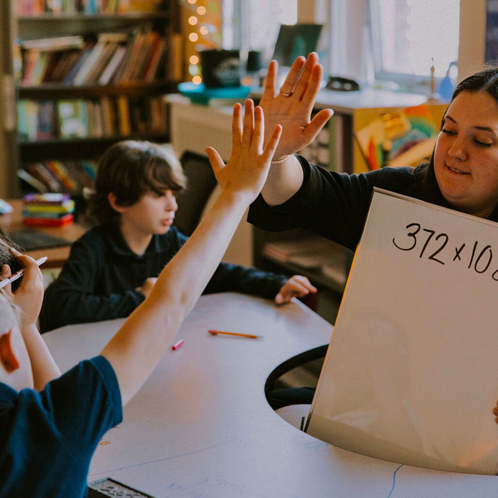 Student and teacher at PCS West tuition-free charter school high five across a classroom table.