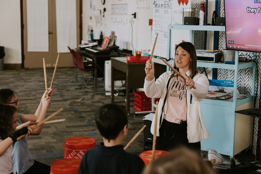 “teacher at tuition-free Provident Charter West teaching drum class to students with drum sticks”