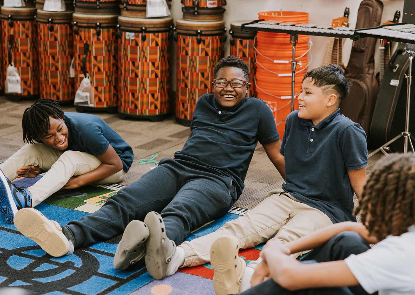Three students at Provident Charter Schools laughing together while seated on the floor of the school music room.