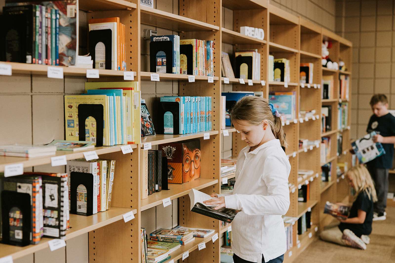 Students looking at books on school library bookshelves at PCS charter school.